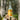 A bottle of Birch Brew Lemon Ginger fermented birch sap drink stands on a cut tree stump outdoors, with a blurred forest background.